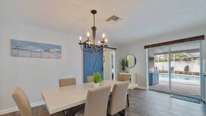 A dining area with a white table, beige chairs, a chandelier, and a view of a pool through glass doors.