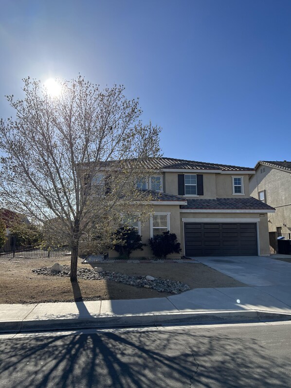 A residential house with a garage, a small front yard with a tree, and a clear blue sky.