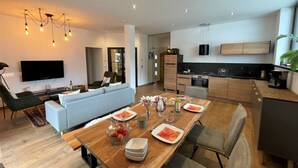 A modern living space with a dining area, kitchen, and a TV mounted on the wall. - Cosy apartment for 4 people with WIFI, TV and terrace (Wildschönau)
