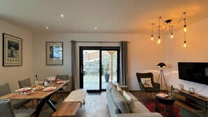 A modern living room with a dining area, a sofa, a TV, and a large window with a view of the outside. - Cosy apartment for 4 people with WIFI, TV and terrace (Wildschönau)