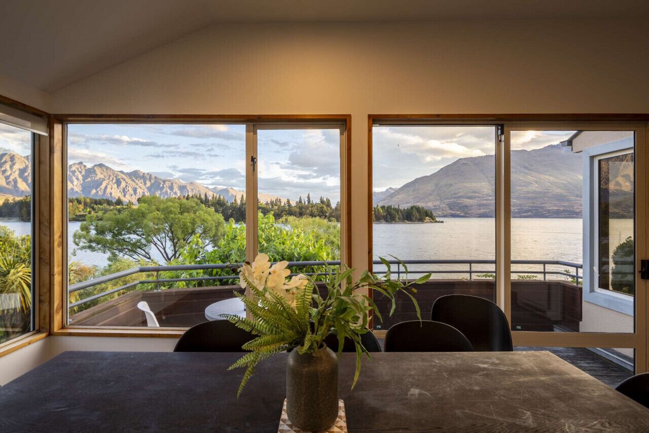 A dining area with a table and chairs, large windows with a mountain and lake view, and a potted plant on the table.