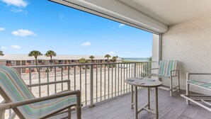 Een balkon met uitzicht op het strand, een zwembad en een gebouw met palmbomen.