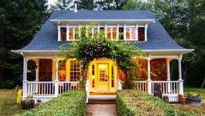 A two-story house with a front porch, a covered entryway, and a garden pathway leading to the door. - Chalet In Trinidad: There is no place quite like it! (Trinidad)