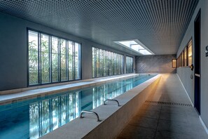 Ein langer, überdachter Pool mit klaren Glaswänden, einem gefliesten Boden und einer Decke mit Gitterstruktur.