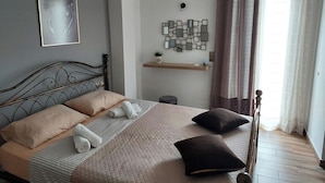 A neatly made bed with pillows and a blanket, a wall-mounted abstract art piece, a small shelf with a plant, and a window with curtains.