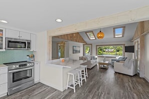 A modern kitchen with a central island, a dining area with a sofa and chairs, and a large window with a view.