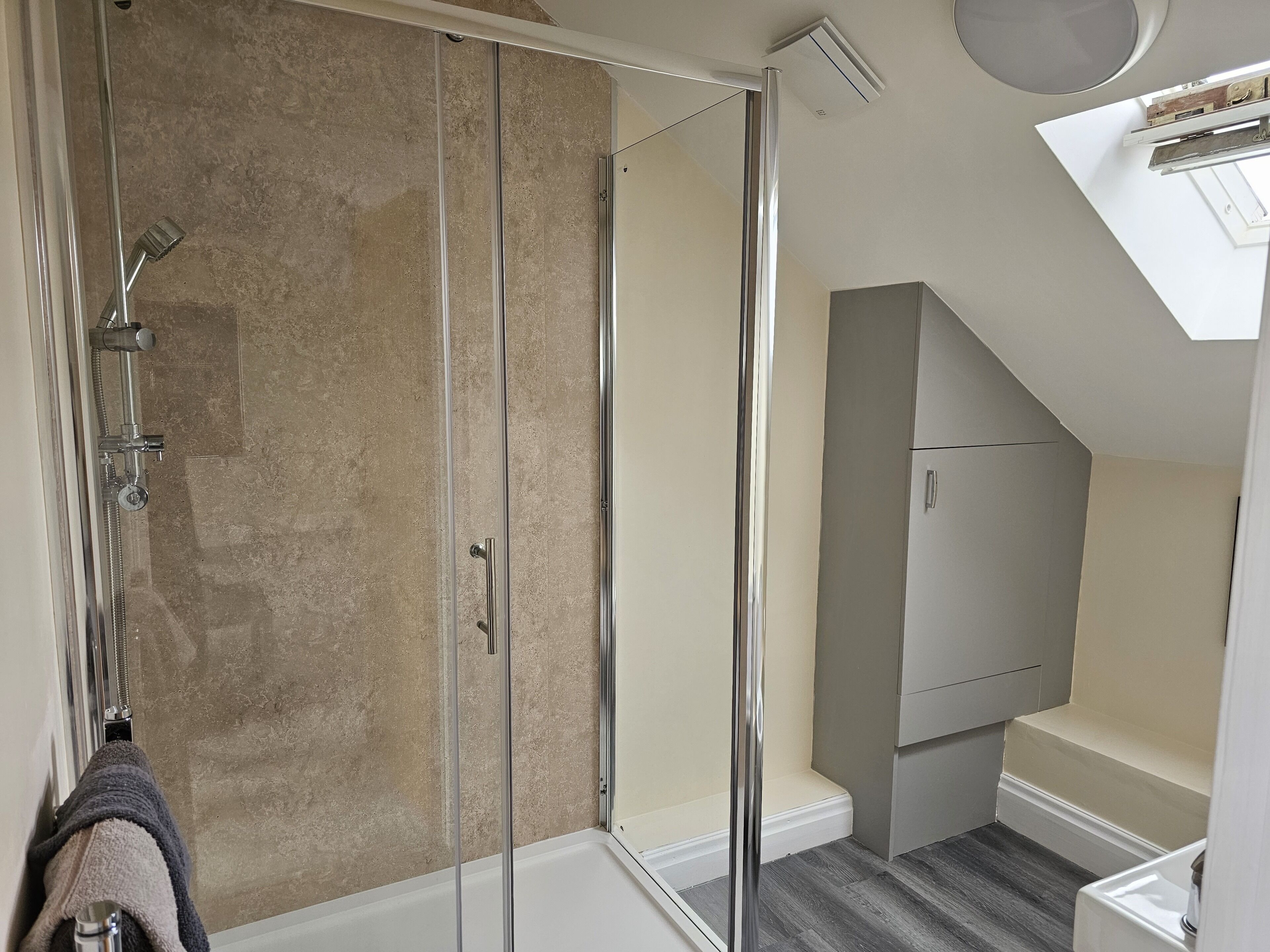 A modern bathroom with a glass shower enclosure, a white bathtub, and a grey cabinet.
