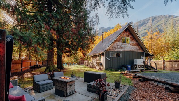 Een rustieke hut met een terras, meubels van riet en een vuurkuil.