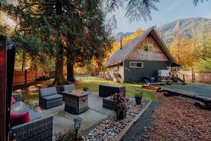 Een rustieke hut met een terras, meubels van riet en een vuurkuil.