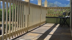 Een overdekt terras met houten leuning, stenen vloer en uitzicht op bergen en groen.