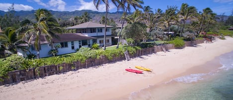 Una propiedad frente a la playa con una casa, una cerca de madera y dos kayaks en la arena.