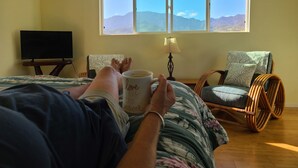 Een kamer met een bed, een televisie, een raam met uitzicht op de bergen, een stoel en een lamp.