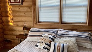 Ein Blockhaus-Zimmer mit Bett, Holzwänden und einem Fenster mit Jalousien.