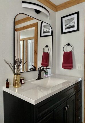 A bathroom with a white sink, black cabinets, a gold vase, and a mirror with a black frame. - Cozy Lazy Dog Cabin (Red Lodge)