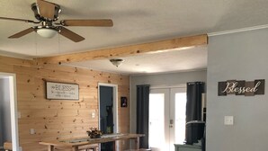 A spacious living area with a wooden floor, a ceiling fan, a bench, and a kitchen area with a window.