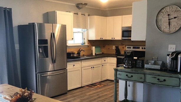 A modern kitchen with stainless steel appliances, white cabinets, a wooden dining table, and a vintage-style coffee station.
