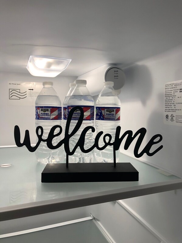 A welcome sign with three bottles of water labeled 'Purified Drinking Water' on a glass counter.