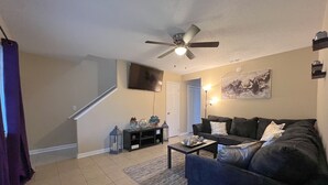 A living room with a dark-colored sofa, a coffee table, a TV, and a ceiling fan. - Charming  and cozy 2 bedroom apartment minutes from Ft. Jackson and VA Hospital (Columbia)