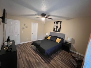 Quarto com cama, ventoinha no teto, porta e parede com objeto decorativo.