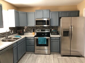 A modern kitchen with grey cabinets, stainless steel appliances, and a tiled backsplash.