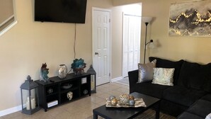 A living room with a black sofa, a coffee table with decorative items, a black entertainment unit, and a mounted TV. - Charming  and cozy 2 bedroom apartment minutes from Ft. Jackson and VA Hospital (Columbia)