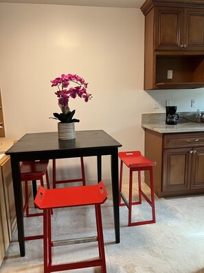 Une cuisine avec une table à manger, deux tabourets rouges, une machine à café et une orchidée en pot.
