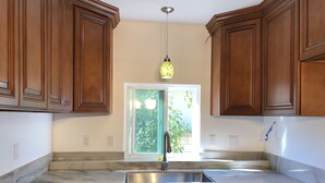 A kitchen with wooden cabinets, a marble countertop, a stainless steel sink, and a hanging light fixture.