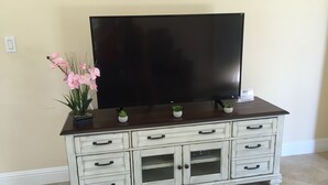 A white wooden TV stand with drawers and a large flat-screen TV.