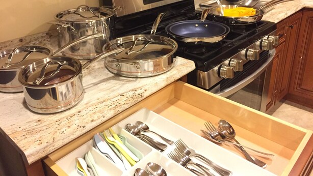 A kitchen with stainless steel cookware, a stove, and a drawer with utensils.