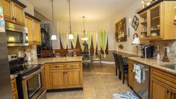 A kitchen with wooden cabinets, a granite countertop, a dining area with chairs, and pendant lighting.