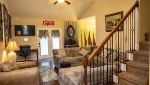 A spacious living room with a sofa, armchair, and a television. A staircase with a wooden railing is visible. - Comfy home in military community (Radcliff)
