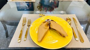 A dining table with yellow plates, gold cutlery, and a clear glass top. - Sweet Home Georgia Amour (Peachtree Corners)