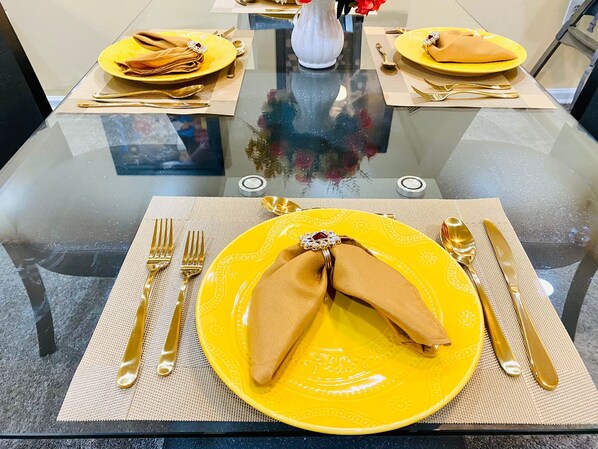 A dining table with yellow plates, gold cutlery, and a clear glass top. - Sweet Home Georgia Amour (Peachtree Corners)