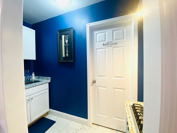 Un baño con una puerta blanca y un espejo enmarcado en la pared.
