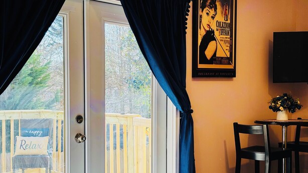 A hotel room with a bed, a desk, and a chair. There is a window with curtains, a poster on the wall, and a view of a deck outside. - Sweet Home Georgia Amour (Peachtree Corners)