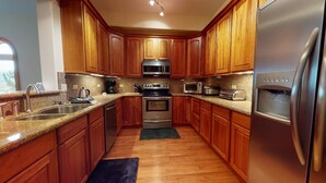 A kitchen with wooden cabinets, stainless steel appliances, granite countertops, and a black rug. - Luxury Condo | Close to Lifts | The Grande 117 (Angel Fire)