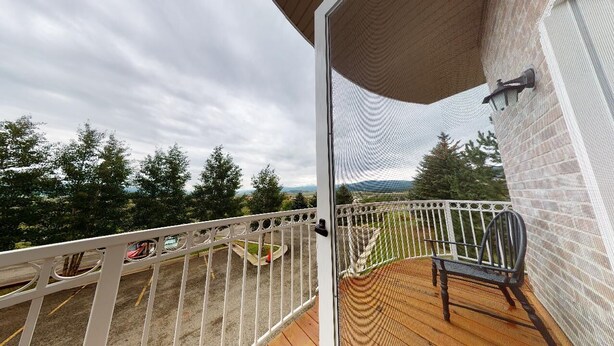 A balcony with a view of trees and mountains, a wooden deck, and a white railing. - Luxury Condo | Close to Lifts | The Grande 117 (Angel Fire)