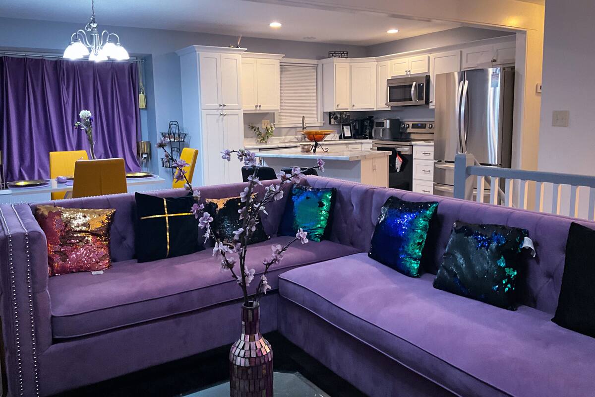 A modern living room with a purple sofa, decorative pillows, and a vase with flowers.