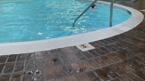 Una piscina interior con agua cristalina, suelo de baldosas y techo alto con conductos a la vista.