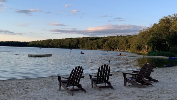 Una playa con tres sillas de madera tipo Adirondack mirando al agua.