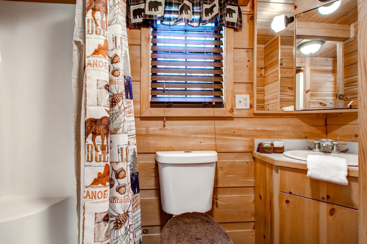 Baño de cabaña de madera con inodoro, lavamanos y cortina de ducha con estampados de fauna.