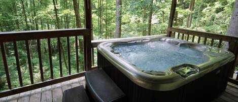 Un jacuzzi en una terraza de madera con vistas a un bosque.