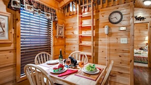 Een houten interieur met een eettafel gedekt voor twee personen, inclusief een fles, wijnglazen en schalen met druiven en aardbeien.
