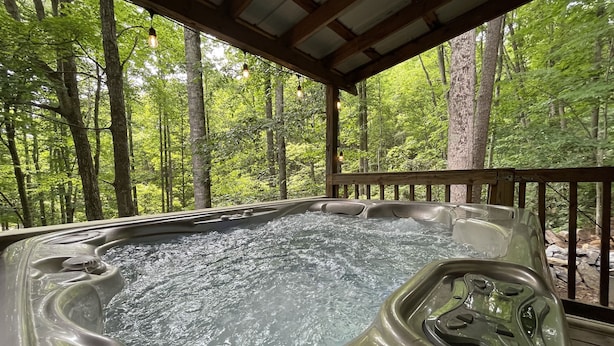 Een hottub in een bebost gebied met een houten terras en metalen leuning.