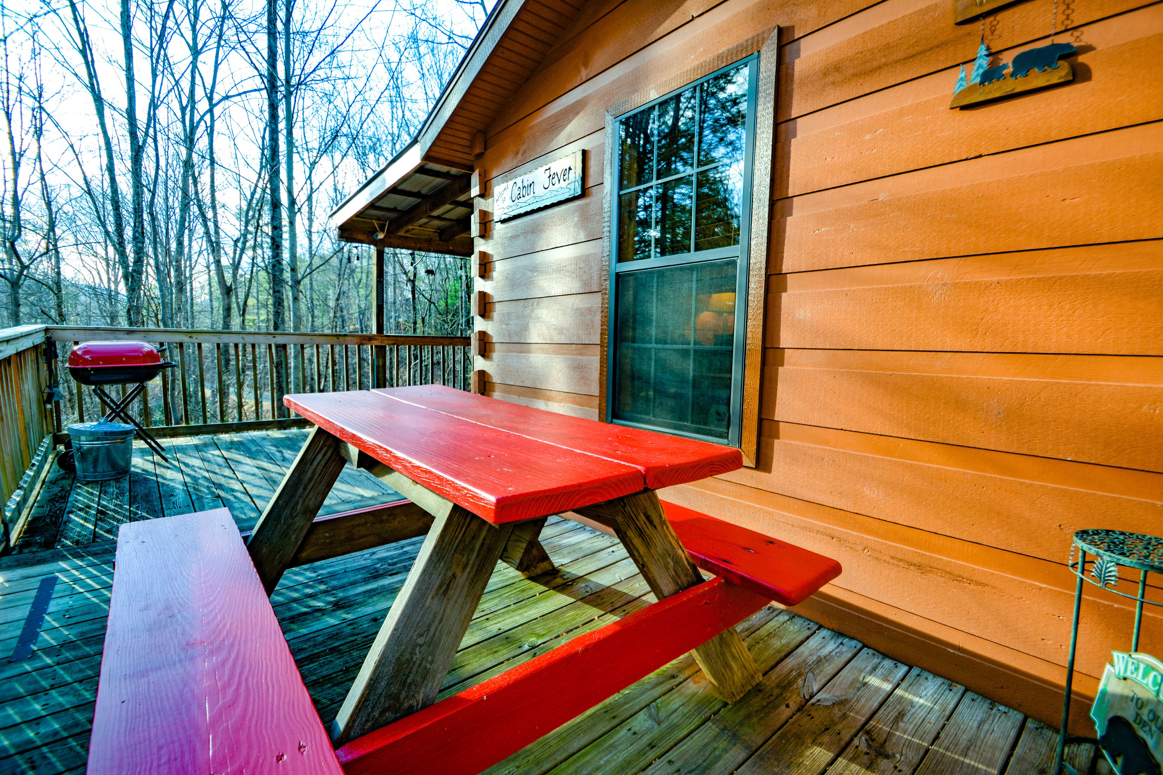 A wooden cabin with a picnic table and a grill on the deck.