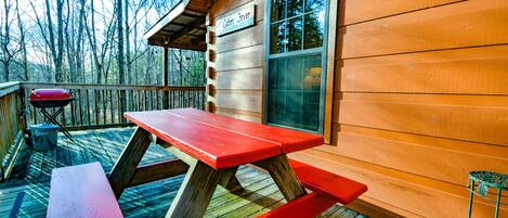 A wooden cabin with a picnic table and a grill on the deck.