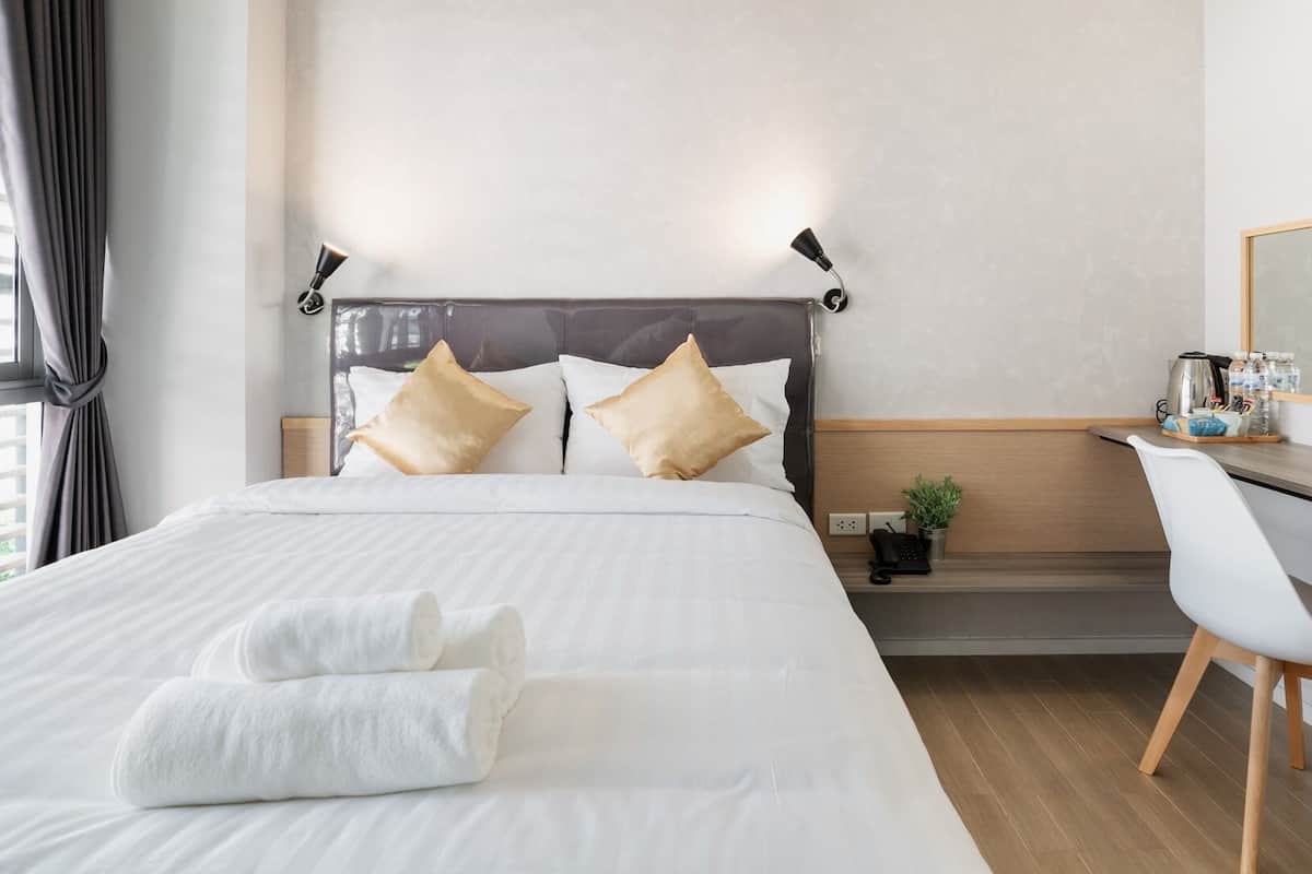 A neatly arranged hotel room with a large bed, a desk with a chair, and a mirror.