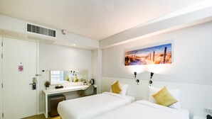 A hotel room with two beds, a desk, a mirror, and a beach scene painting. - Kitzio House Hotel (Bangkok)