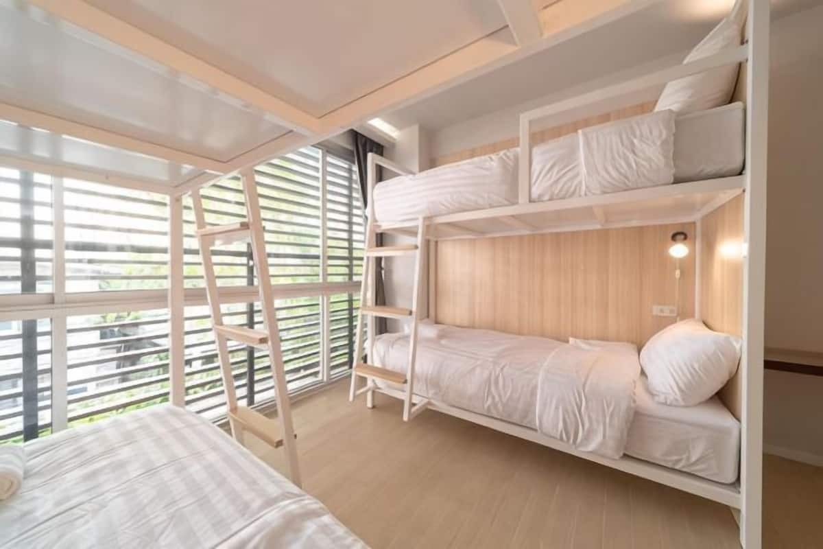 A bunk bed room with a ladder, wooden flooring, and a window with blinds.