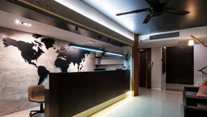 A modern reception area with a world map on the wall, a reception desk, and a staircase leading to an upper level. - Kitzio House Hotel (Bangkok)